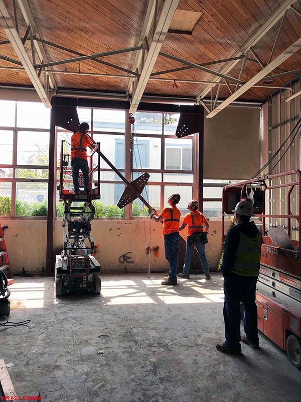 workers are lifting steel into place in front of windows