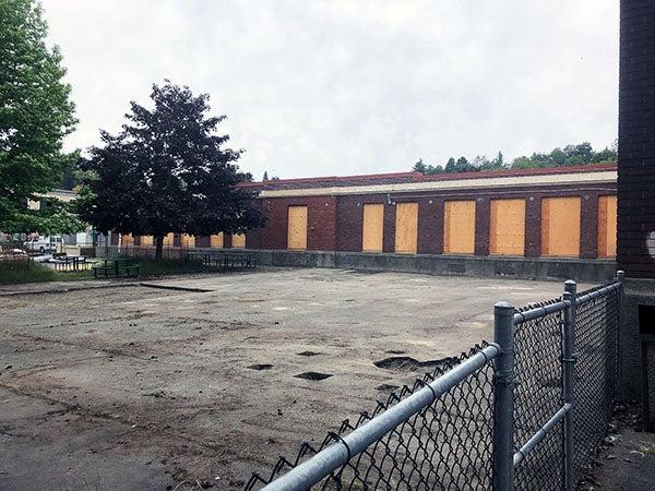 a concrete area in front of a brick building with boarded up windows