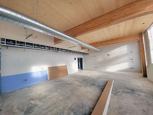 a large room with wood beams and a wood celing has unfinished walls and floor with a metal duct near the ceiling