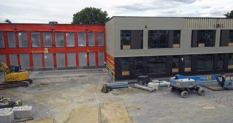 a building with metal siding and windows on part and orange underlayment and plastic in the window openings on another part