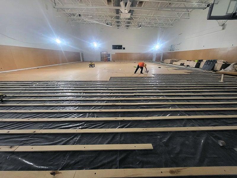 a large room with high ceilings has a worker installing wood planks for a floor