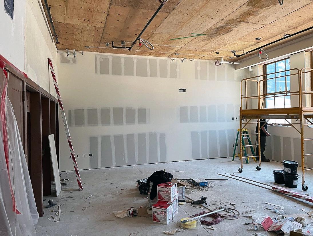 a room has a wood ceiling. the walls are wallboard with tape and mud installed. There is a window on the right and doors on the left